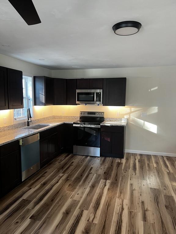 kitchen with light stone countertops, appliances with stainless steel finishes, sink, and hardwood / wood-style floors