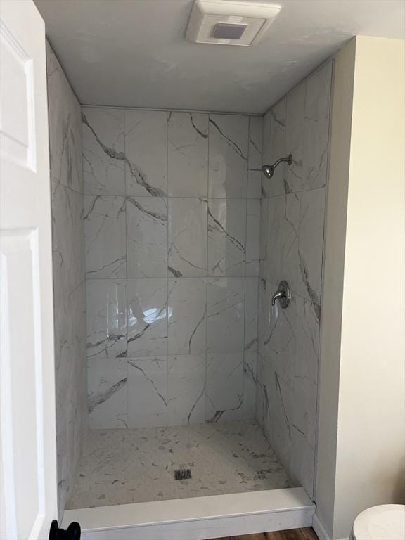 bathroom with toilet, a tile shower, and hardwood / wood-style floors