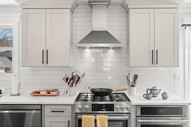 kitchen featuring decorative backsplash, appliances with stainless steel finishes, light countertops, and wall chimney exhaust hood