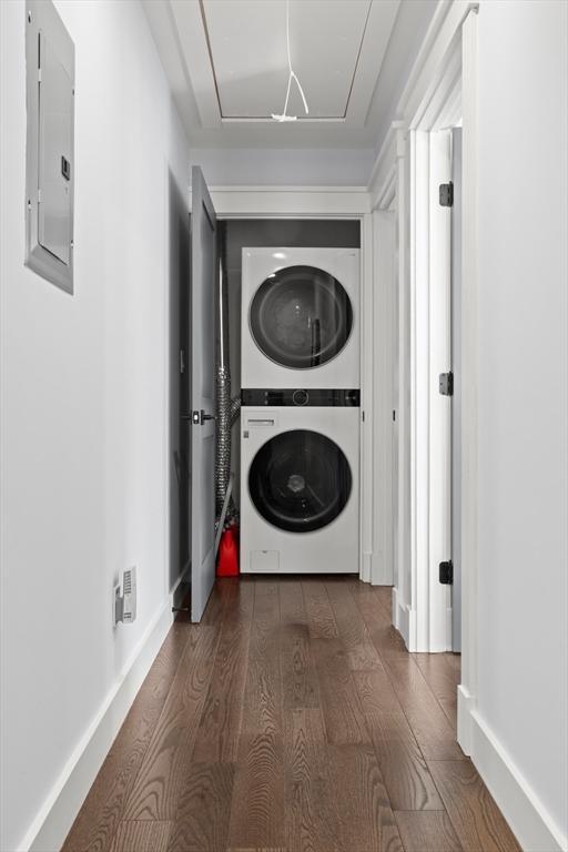 clothes washing area with electric panel, stacked washing maching and dryer, laundry area, attic access, and dark wood-style flooring