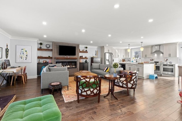 living room with a large fireplace, recessed lighting, crown molding, and dark wood-type flooring