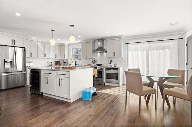 kitchen featuring beverage cooler, appliances with stainless steel finishes, dark wood-style floors, wall chimney exhaust hood, and a sink