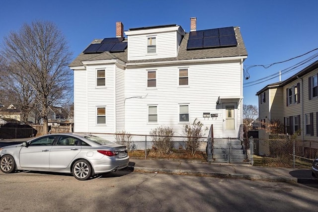 43 Huntington St, Brockton, MA 02301 - rear view of property featuring roof mounted solar panels, a gate, a chimney, and a shingled roof