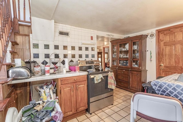 43 Huntington St, Brockton, MA 02301 - kitchen with stainless steel electric range, tile counters, light tile patterned flooring, backsplash, and glass insert cabinets