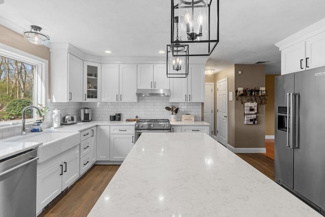 kitchen with a sink, under cabinet range hood, light stone countertops, and stainless steel appliances