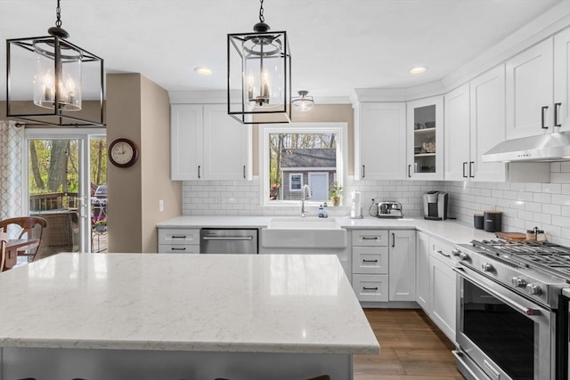 kitchen featuring stainless steel appliances, a sink, light stone counters, a notable chandelier, and under cabinet range hood