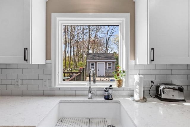 interior details with a sink, white cabinetry, light stone countertops, and tasteful backsplash