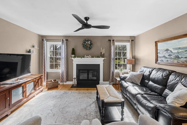 living room featuring a fireplace with flush hearth, baseboards, ceiling fan, and wood finished floors
