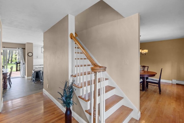 staircase with a baseboard heating unit, baseboards, an inviting chandelier, and wood finished floors