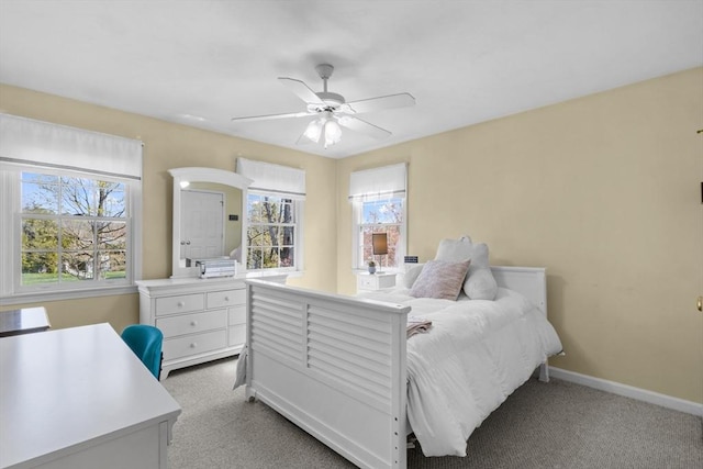 bedroom with baseboards, multiple windows, light carpet, and a ceiling fan