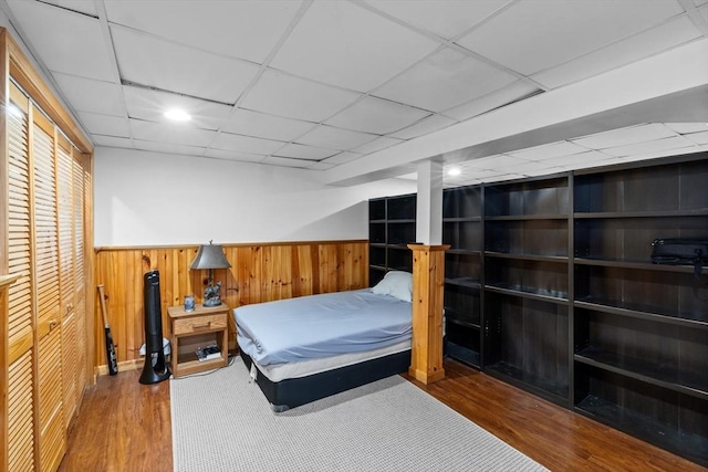bedroom featuring wooden walls, a wainscoted wall, a drop ceiling, and wood finished floors