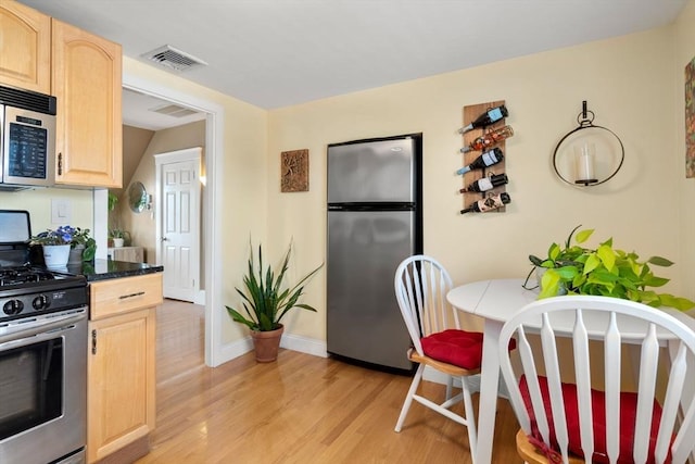 247 Ash St Unit 3, Waltham, MA 02453 - kitchen with appliances with stainless steel finishes, light brown cabinetry, light wood-style flooring, baseboards, and dark countertops