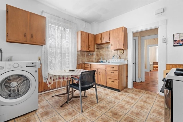 kitchen with light tile patterned floors, brown cabinetry, gas range, washer / clothes dryer, and light countertops