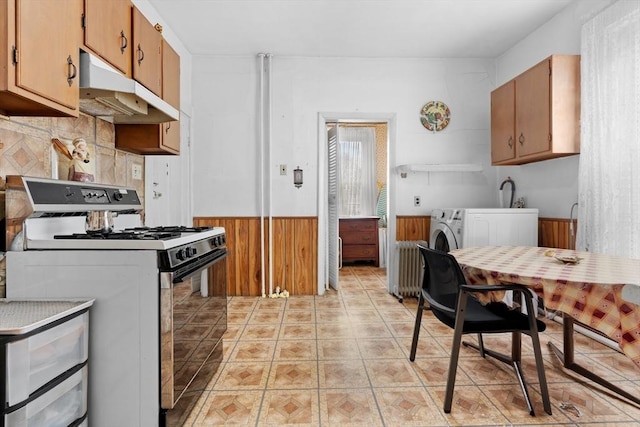 kitchen featuring light tile patterned floors, under cabinet range hood, a wainscoted wall, independent washer and dryer, and gas range oven