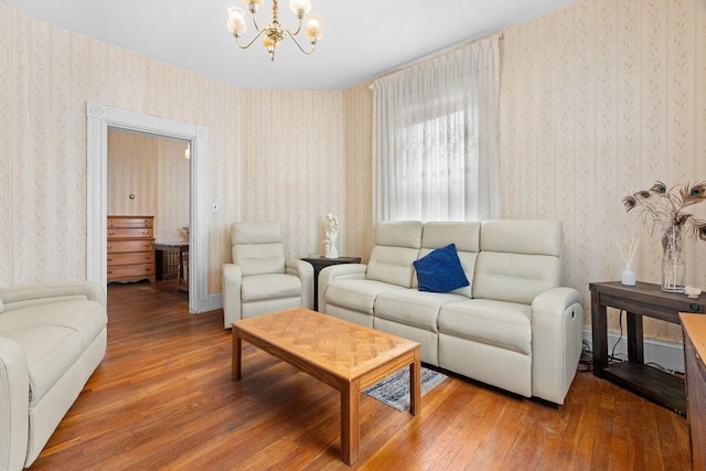 living room featuring wallpapered walls, a notable chandelier, baseboards, and wood finished floors