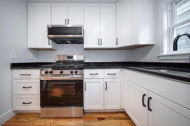 121 Horton St, Fall River, MA 02723 - kitchen featuring stainless steel appliances, a sink, white cabinets, light wood finished floors, and dark countertops