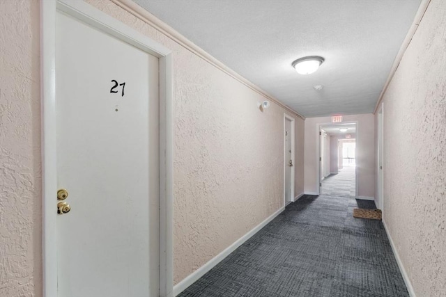 corridor with baseboards, dark carpet, and a textured wall