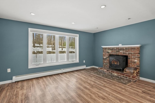 unfurnished living room featuring hardwood / wood-style floors, a baseboard radiator, and a wood stove