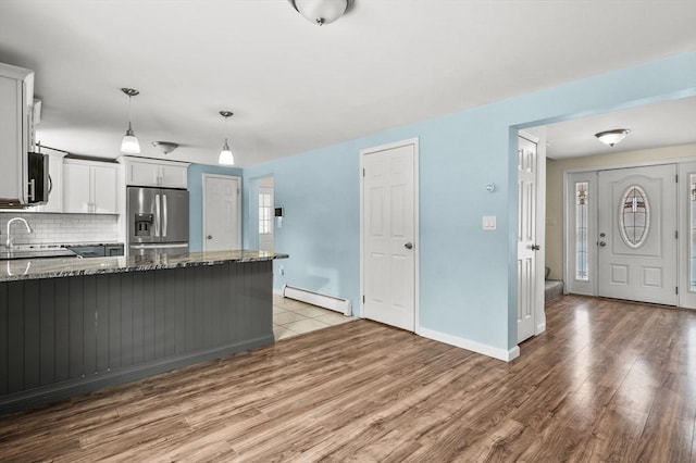 kitchen with pendant lighting, appliances with stainless steel finishes, dark stone countertops, decorative backsplash, and a baseboard radiator