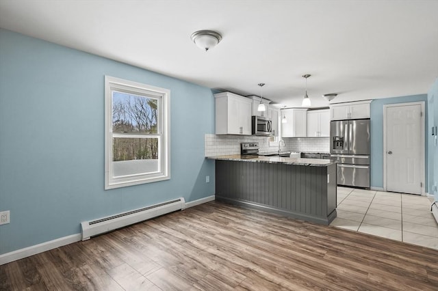 kitchen featuring pendant lighting, appliances with stainless steel finishes, baseboard heating, white cabinets, and kitchen peninsula