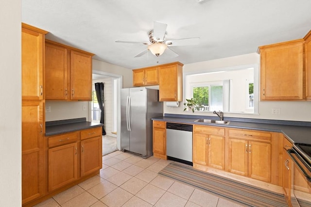kitchen with appliances with stainless steel finishes, a sink, ceiling fan, dark countertops, and light tile patterned floors