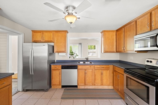 kitchen with stainless steel appliances, a sink, dark countertops, a ceiling fan, and light tile patterned flooring