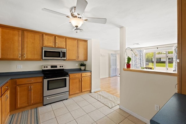 kitchen with appliances with stainless steel finishes, brown cabinetry, dark countertops, and a ceiling fan