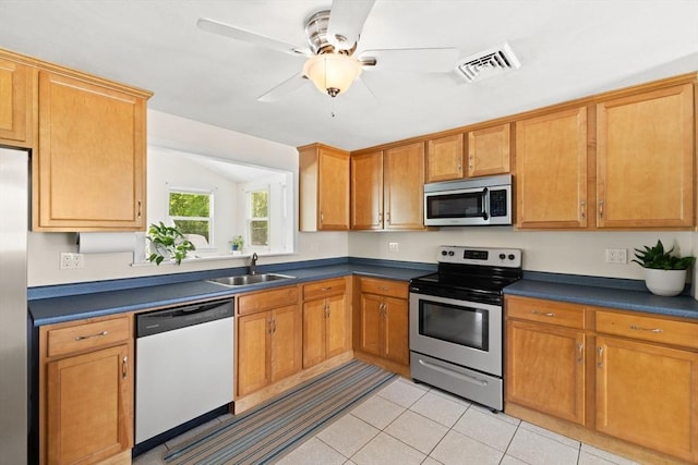 kitchen featuring stainless steel appliances, a sink, dark countertops, light tile patterned floors, and brown cabinets
