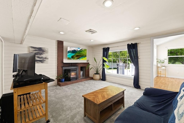 living area featuring healthy amount of natural light, a fireplace, wood walls, recessed lighting, and carpet floors
