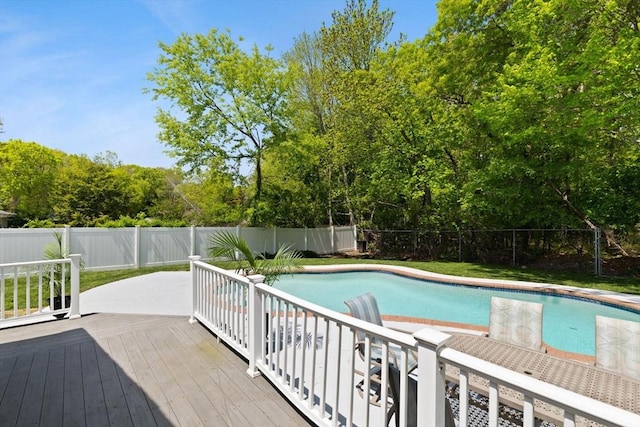 view of pool with a fenced backyard, a deck, and view of scattered trees