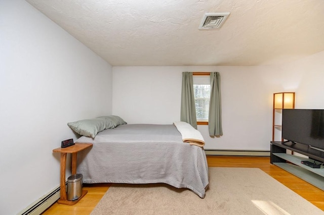 bedroom with a textured ceiling, baseboard heating, and light hardwood / wood-style flooring