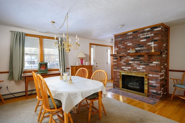 dining room with an inviting chandelier, a brick fireplace, light hardwood / wood-style flooring, a textured ceiling, and a baseboard heating unit