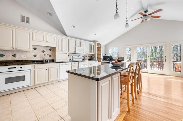 kitchen with visible vents, a breakfast bar, decorative backsplash, white appliances, and a sink