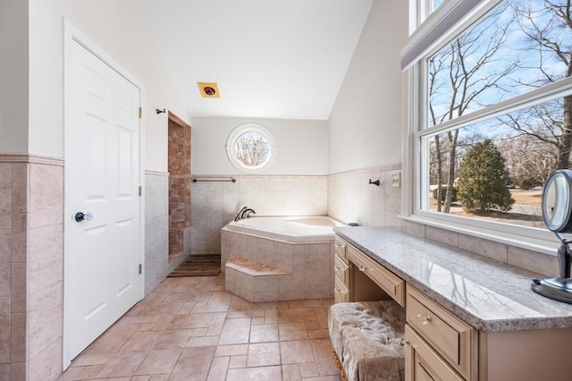 full bath with stone tile floors, a wainscoted wall, lofted ceiling, a garden tub, and tile walls