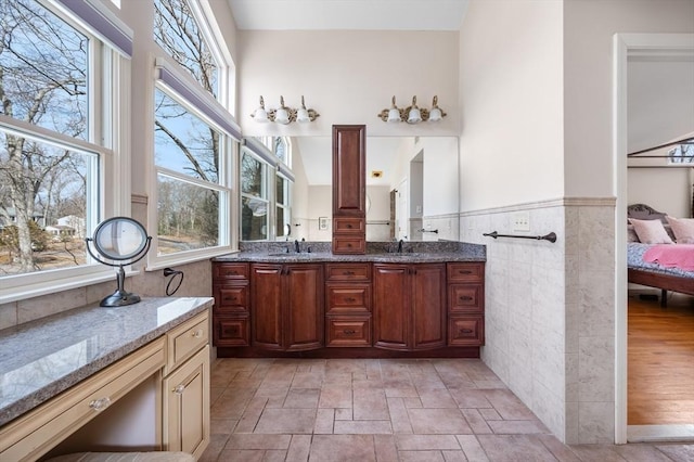 ensuite bathroom featuring a wainscoted wall, double vanity, a sink, ensuite bathroom, and tile walls