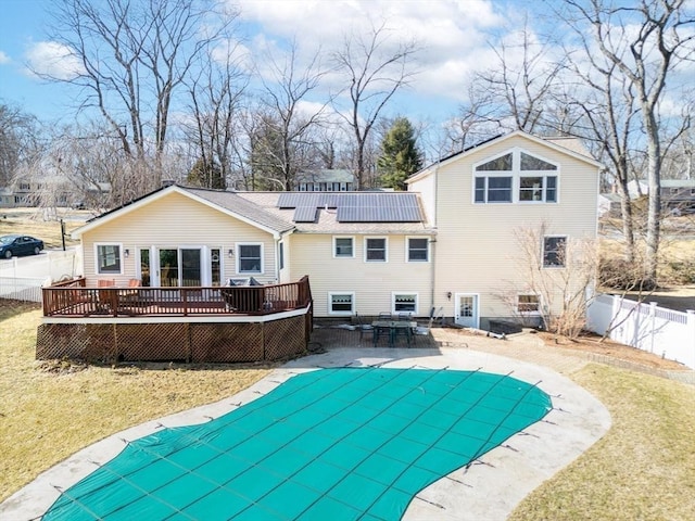 rear view of property featuring a fenced in pool, a wooden deck, solar panels, a yard, and a fenced backyard