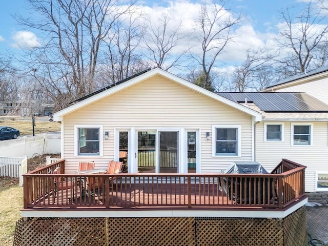 back of house with roof mounted solar panels, a wooden deck, and fence