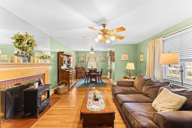 living area with ceiling fan, wood finished floors, a wood stove, and baseboards