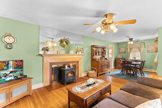 living room with a baseboard heating unit, a wood stove, baseboards, and hardwood / wood-style floors