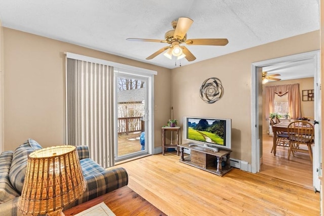 living area with a ceiling fan, light wood-style flooring, baseboards, and a textured ceiling