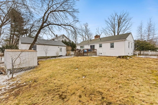 rear view of house with an outbuilding, a chimney, a lawn, fence, and a wooden deck