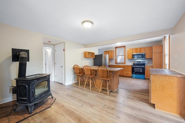 kitchen with tile countertops, light hardwood / wood-style flooring, a kitchen breakfast bar, a wood stove, and stainless steel appliances