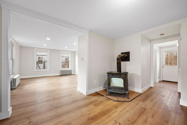 unfurnished living room with a wood stove, radiator, and light wood-type flooring