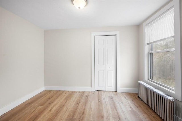 unfurnished bedroom with radiator heating unit, a closet, and light hardwood / wood-style flooring