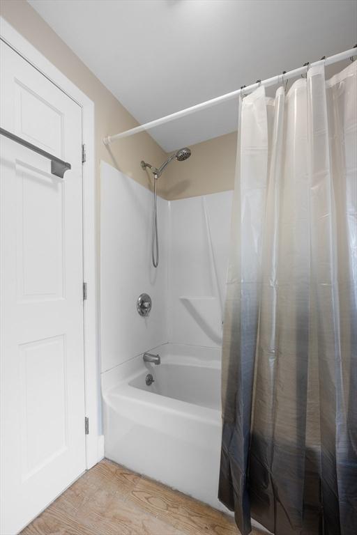 bathroom with wood-type flooring and shower / bathtub combination with curtain