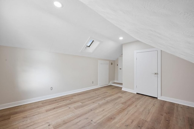 bonus room with lofted ceiling with skylight and light wood-type flooring