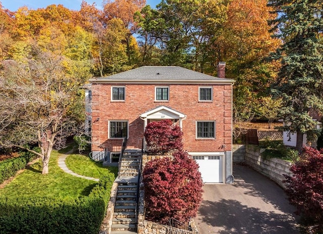 colonial-style house featuring driveway, stairs, a garage, brick siding, and a chimney