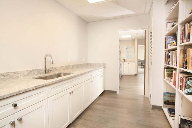 kitchen featuring light stone countertops, light hardwood / wood-style flooring, a drop ceiling, white cabinets, and sink