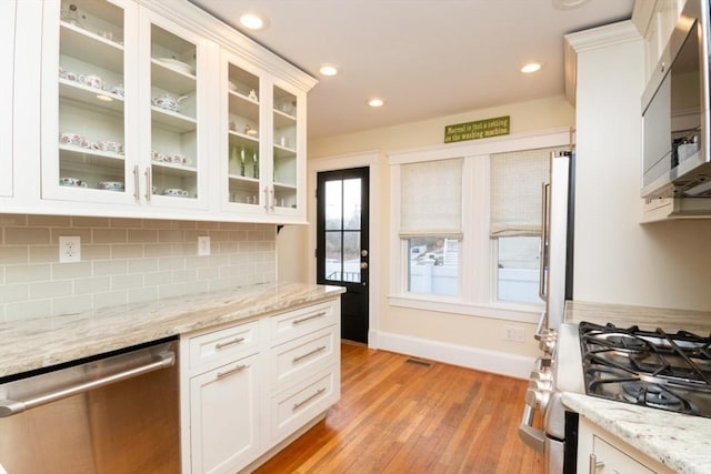 kitchen featuring backsplash, light hardwood / wood-style flooring, light stone countertops, appliances with stainless steel finishes, and white cabinets