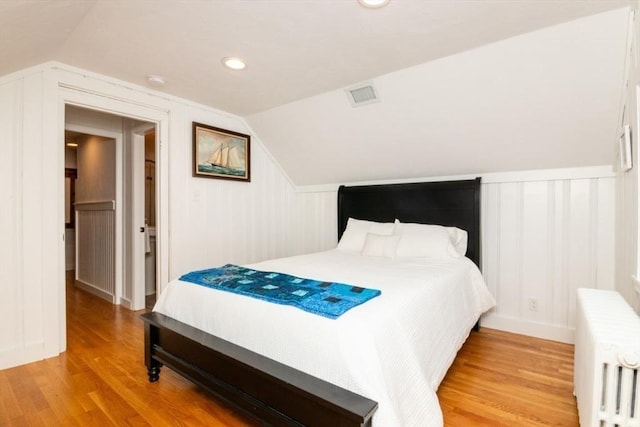 bedroom with light wood-type flooring, radiator heating unit, and vaulted ceiling